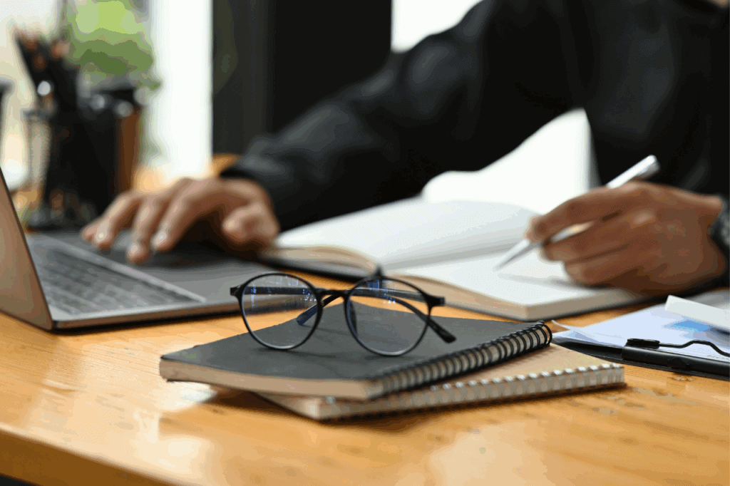 Person with a notepad and pen writing next to a laptop