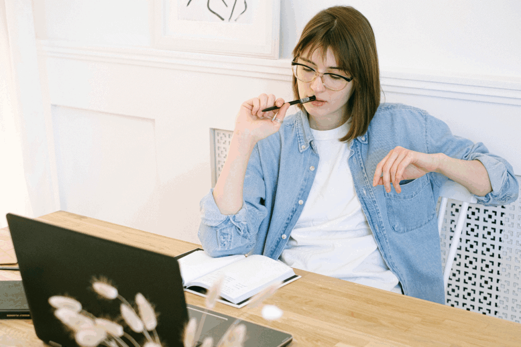 Woman sitting at laptop chewing pen and thinking