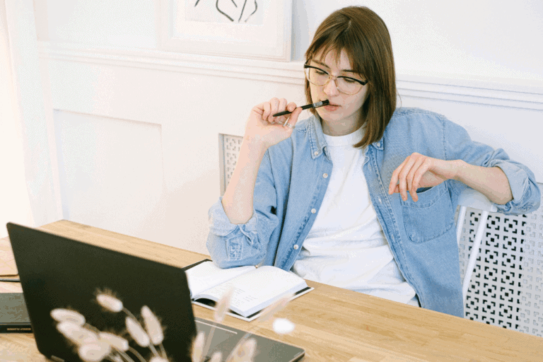 Woman sitting at laptop chewing pen and thinking
