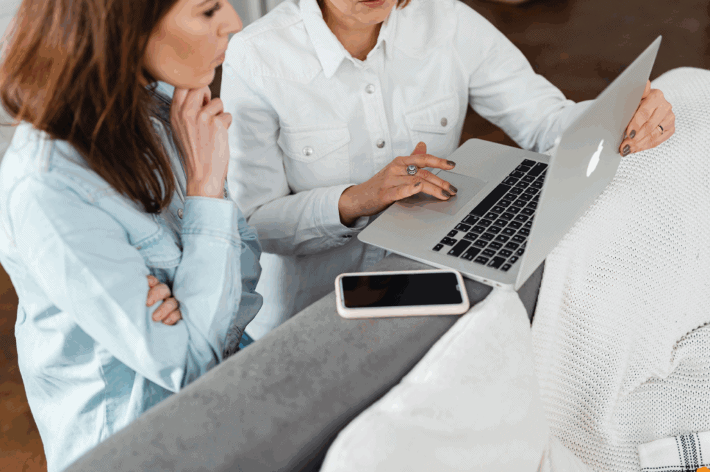 Two people sitting side-by-side on laptops collaborating