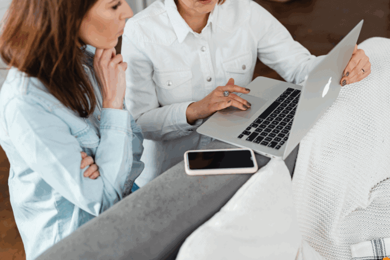 Two people sitting side-by-side on laptops collaborating