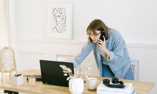 pexels-photo-4240498-4240498 Woman multitasking with laptop and phone in modern home office setting.